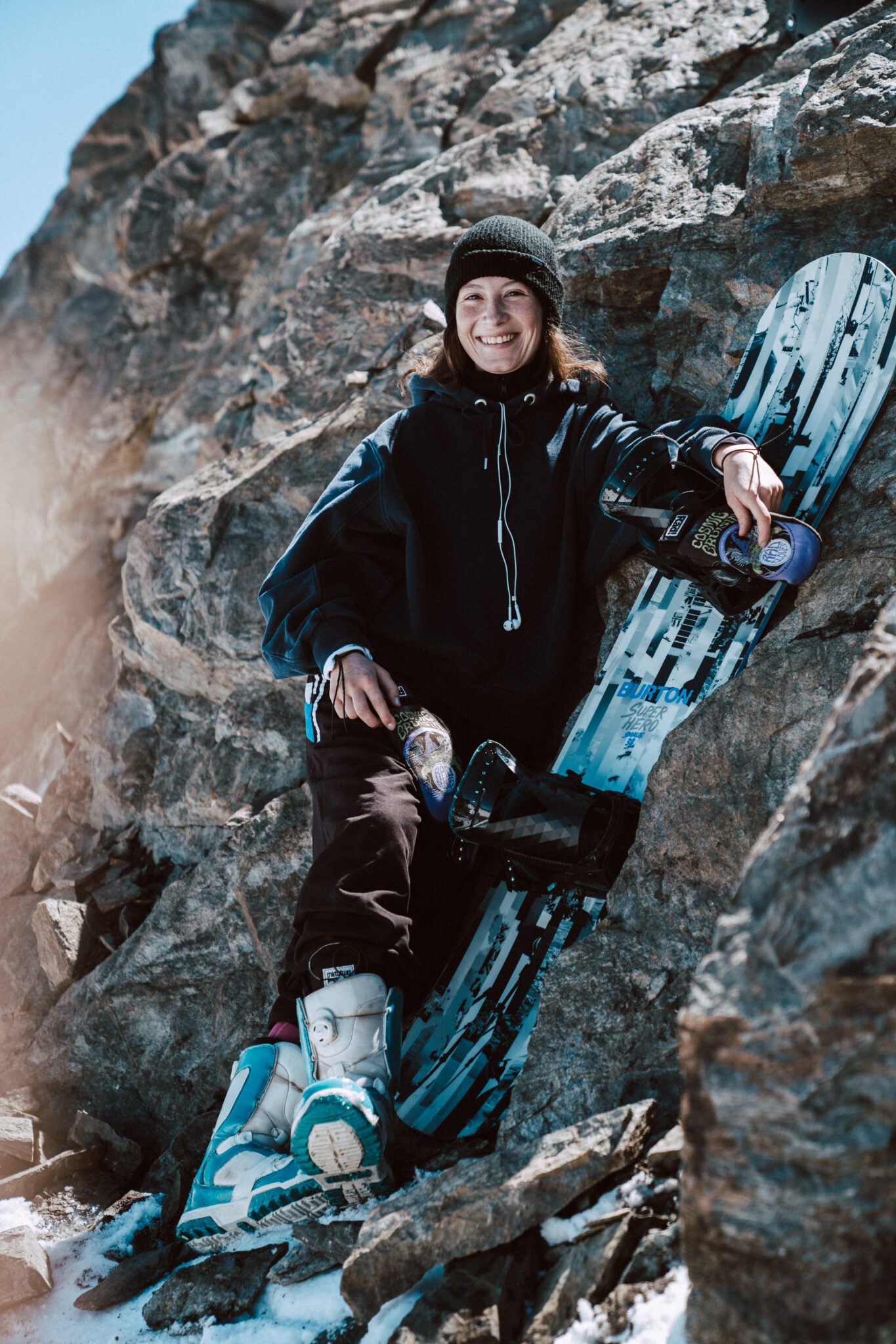 Uśmiechnięta dziewczyna z deską snowboardową na tle skały