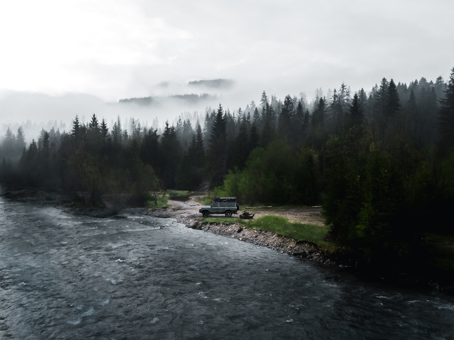 Auto terenowe stojące na brzegu jeziora, w tle las i unosząca się mgła