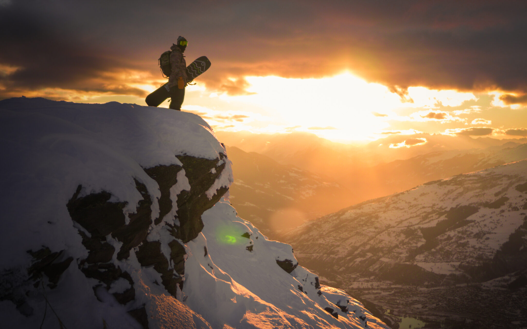 Snowboardzista stojący na skraju góry na tle zachodzącego słońca