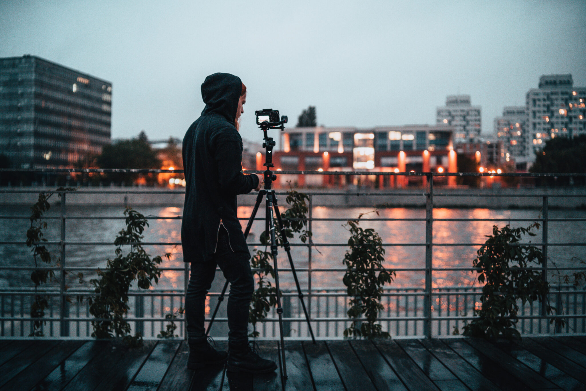 Fotograf robi zdjęcie aparatem na statywie nad brzegiem rzeki z widokiem na miasto