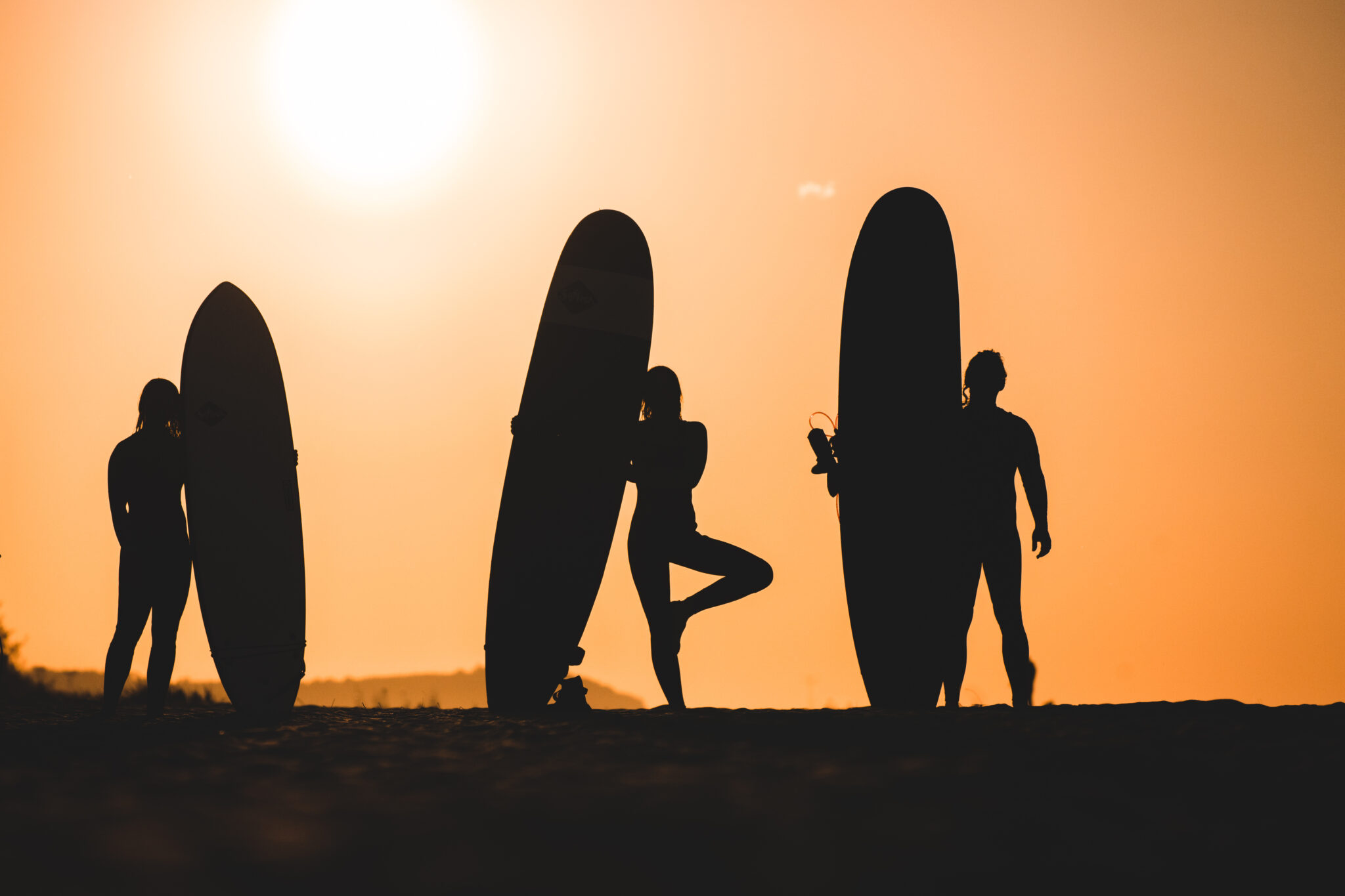Sylwetki 3 surferów na tle zachodzącego słońca